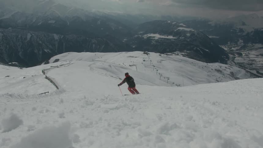 A person skiing down a snowcovered hill and at the base of a region with many mountains