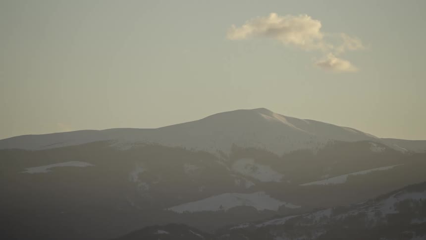 A huge mountain with snow on its surface and a single cloud passing through the sky