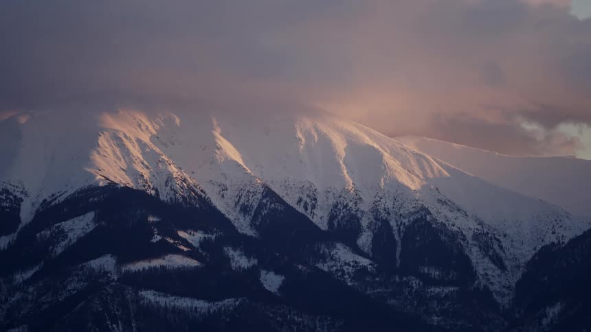 Snowcapped mountains under a soft glowing light from the setting or rising sun