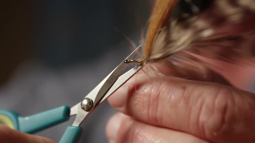 A person is using a pair of scissors to trim a fly fishing lure