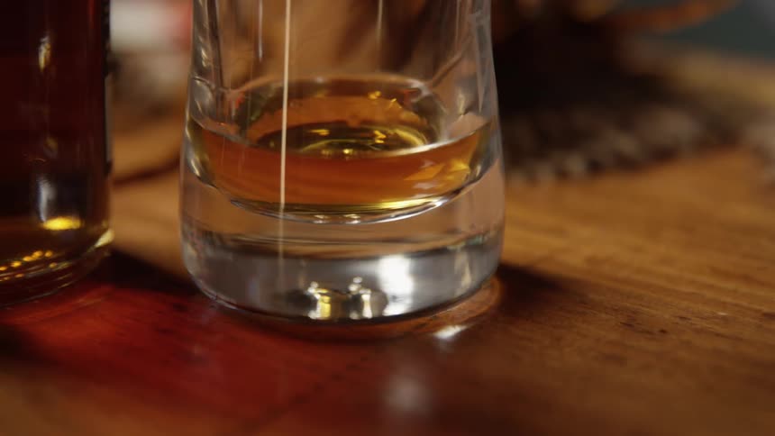 Close up of a hand placing a glass of liquor over a table