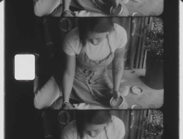 An archival of a woman sitting and placing a pot has grains in a basin