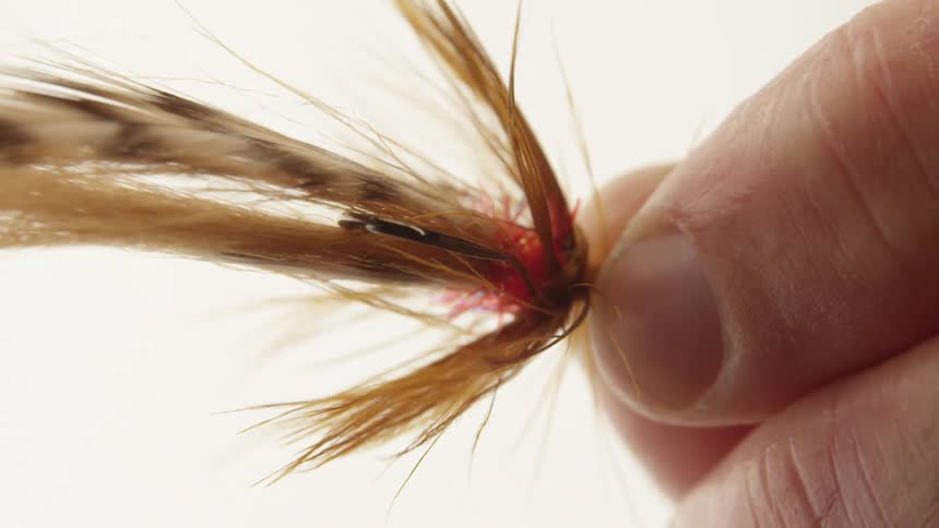 A closeup of a persons fingers holding a fly fishing lure with fine detailed and colorful fibers