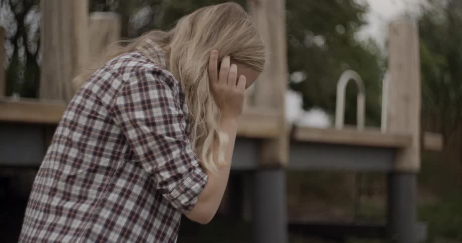 A woman arranging her hair while looking at the ground