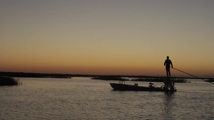 A silhouette of a person on top of a boat and is rowing using a huge oar