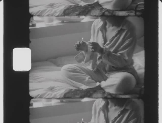 Woman sitting in bed lights a cigarette caught on vintage film