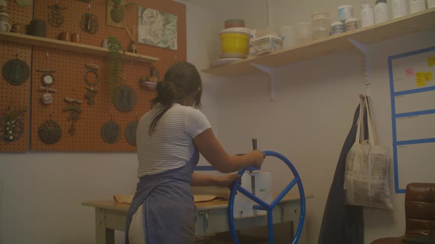 A woman in an apron spins a wheel at a workbench