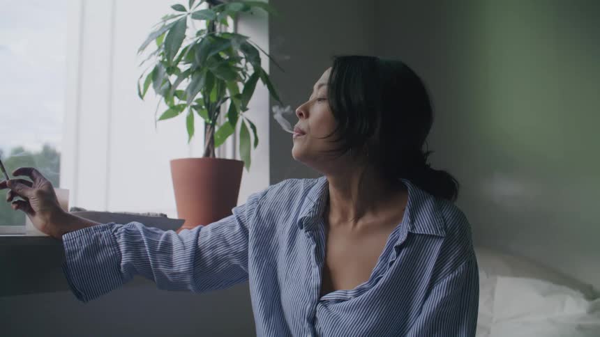 Woman sitting on the sofa in the living room smokes smoking a cigarette