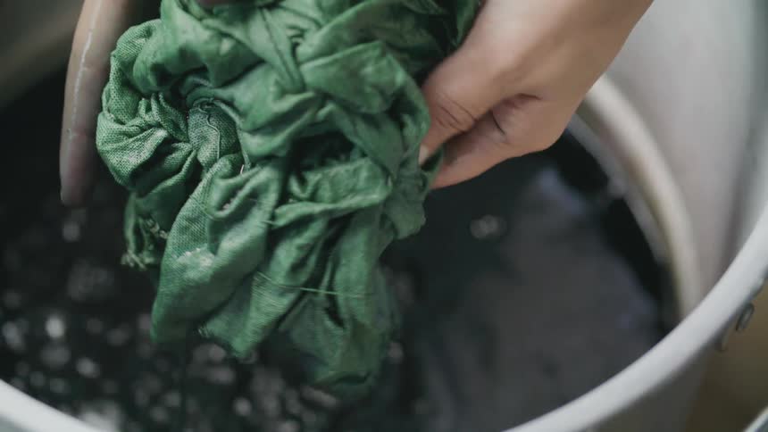 A human hand squeezing a cloth that is filled with ink into a barrel of liquid