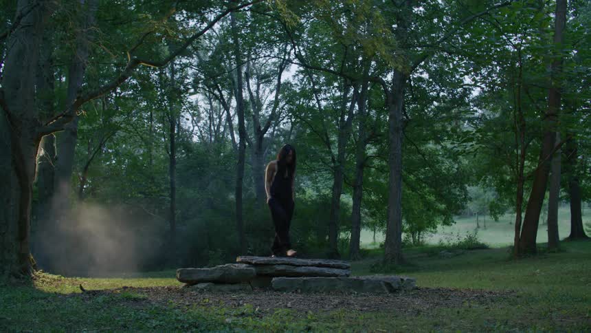 A person walking in an area full of trees and then sitting on a rock