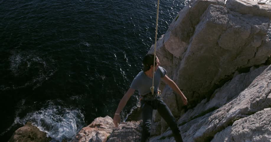 A person is rock climbing above the sea secured with a rope
