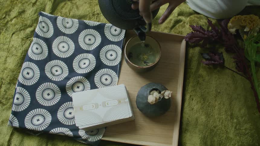 A person is preparing tea with a teapot and other items laid out over a wooden tray