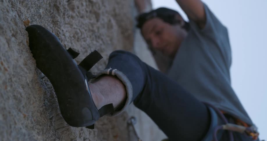 Male rock climber clinging to cliff face descends