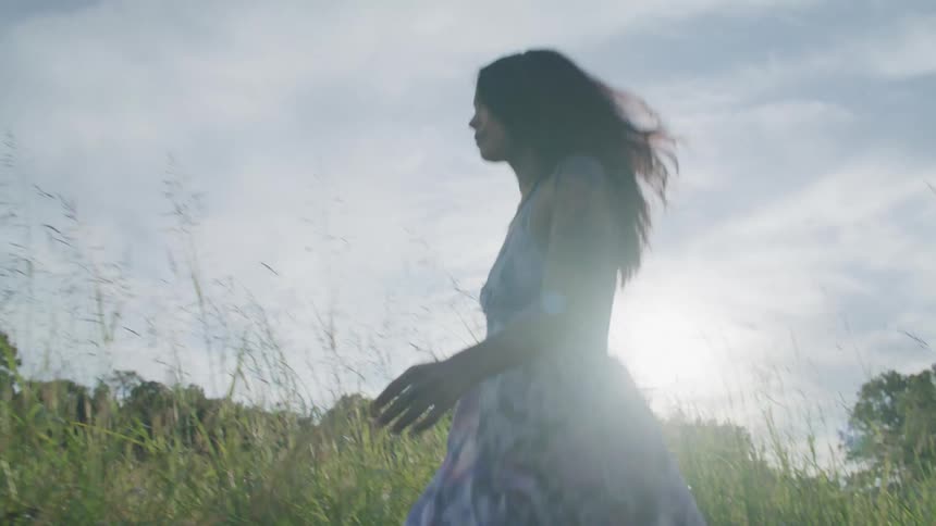 A woman in a floral dress runs in a field of grass at morning