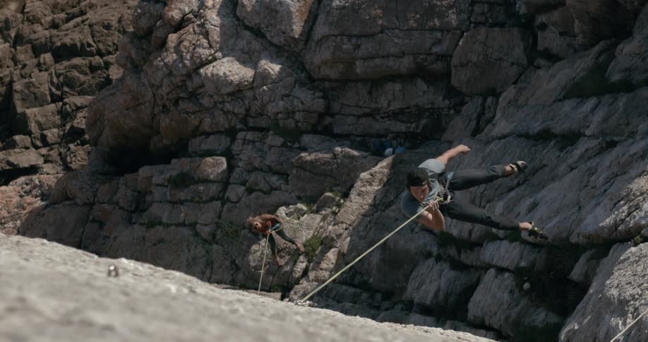 Man outdoors climbing a rock and hanging from a rope during day time