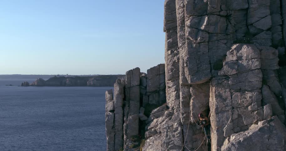 Two people climbing a mountain wall on a cliff by the sea