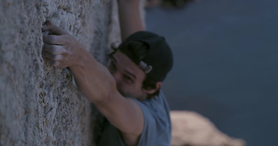A man rock climbing loses his grip onto the surface of a steep cliff