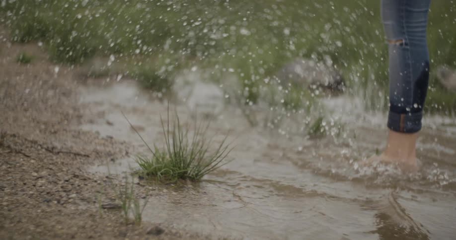 A woman kicks up water as she wades in a pond