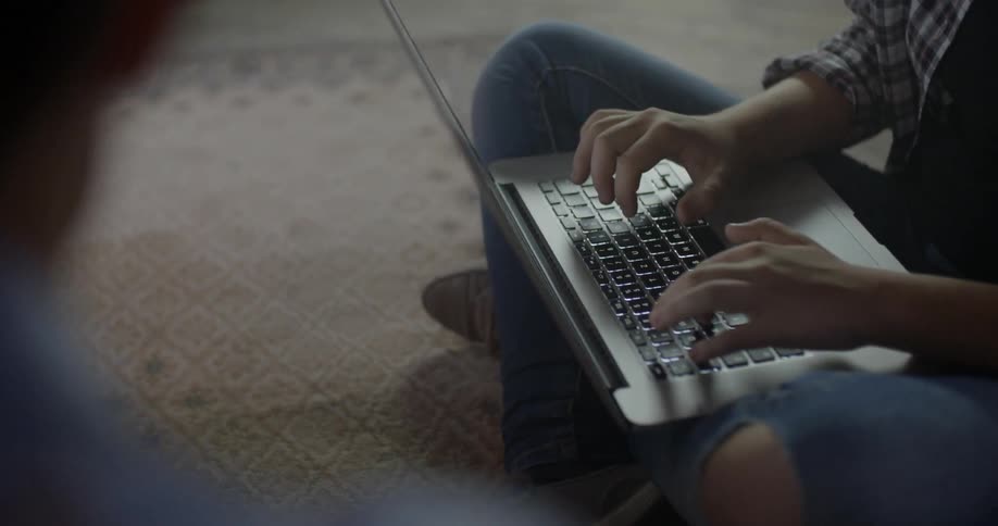 A person sitting on the floor types on a laptop