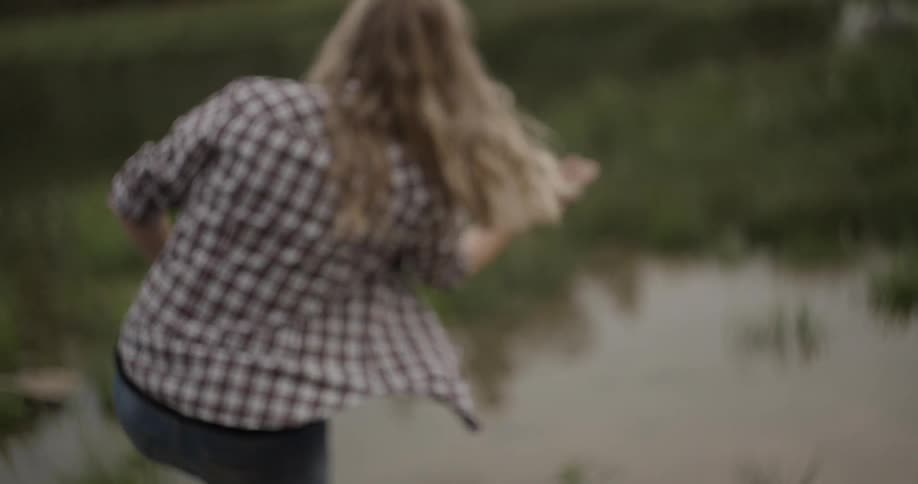 A woman tosses a rock across a pond