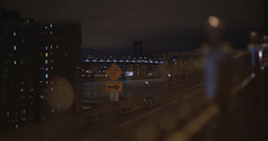 Illuminated city buildings stand beyond a street at night