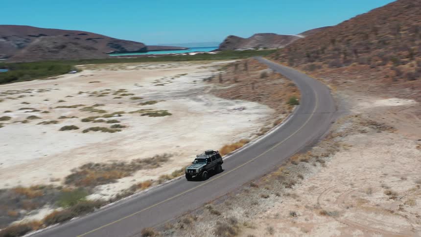 Jeep truck entering a road surrounded by desert mountains with the sea in the background