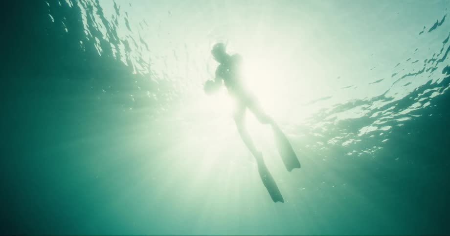 Silhouette of a diver inside the sea with a sun reflection on him