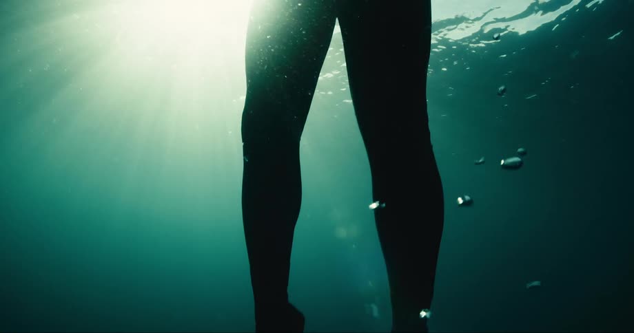 A person in a diving suit is rising to the surface of the water and releasing several bubbles