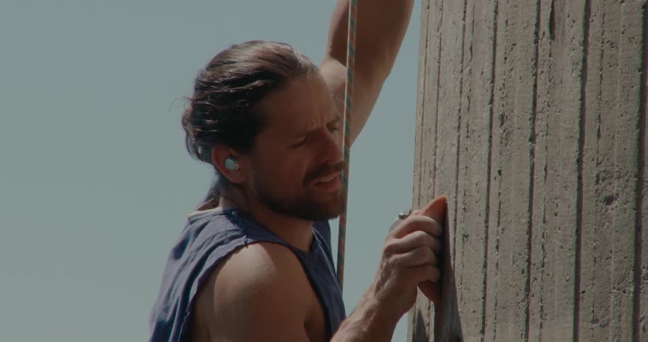 A rock climber reaches for a handhold and looks down before continuing climbing a wall