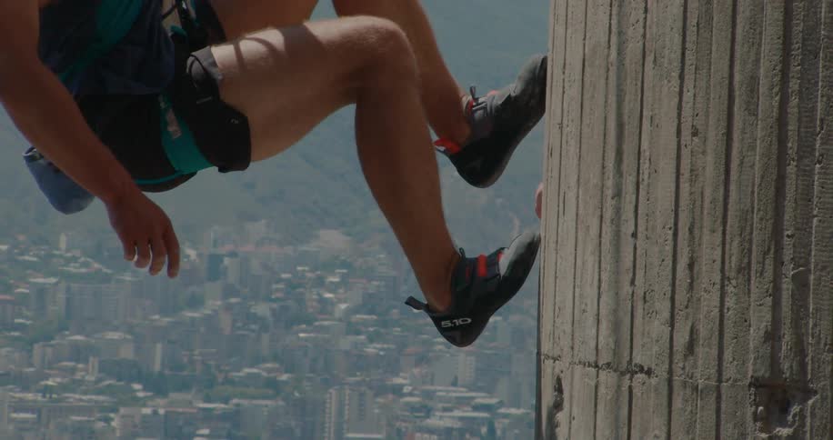 A person lunges with both feet against a wall surface and ends up hanging behind a huge city