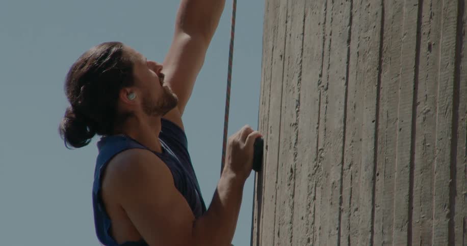 A strong man climbs a wall during a hot day