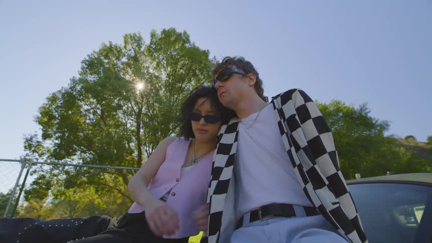 Couple sitting on car near fence on a sunny day cuddle together