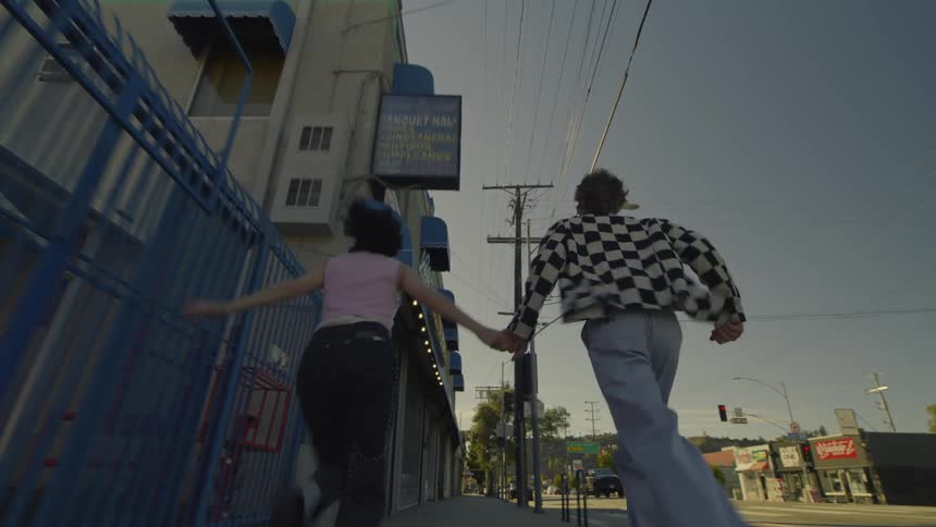 A man and woman run down a sidewalk in a small town