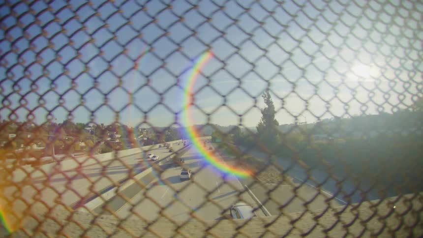 From a net fence we see the highway as cars go back and forth