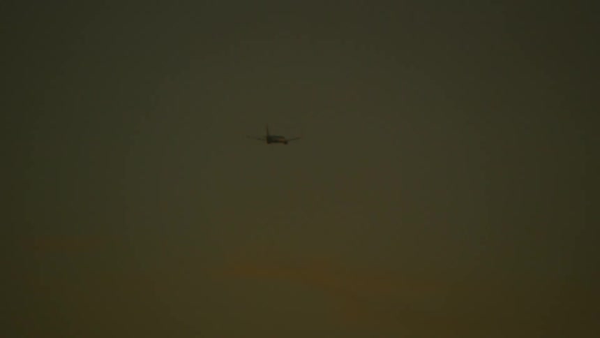 A commercial plane flying over a part of the sea on a morning with an orange sky
