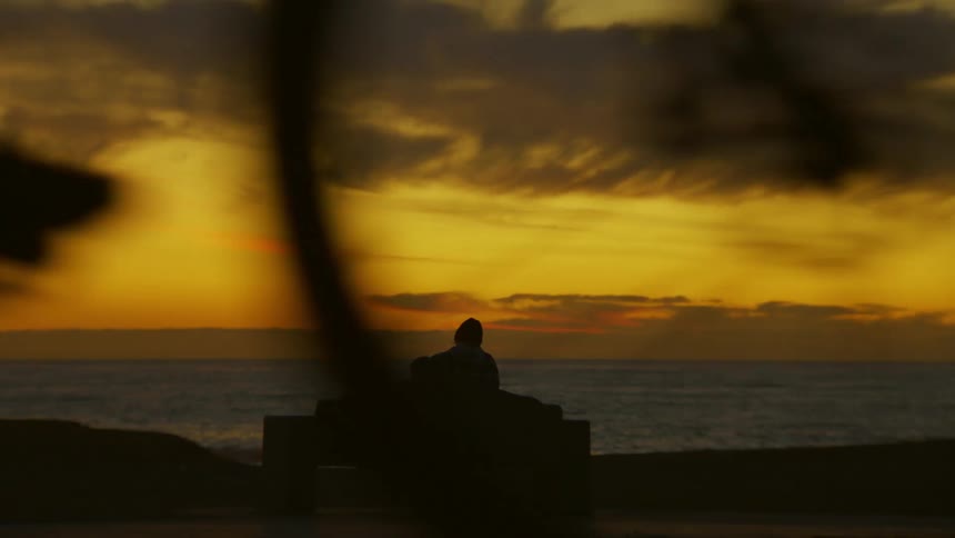 Landscape and silhouette of a man sitting on a bench by the sea against an orange evening sky