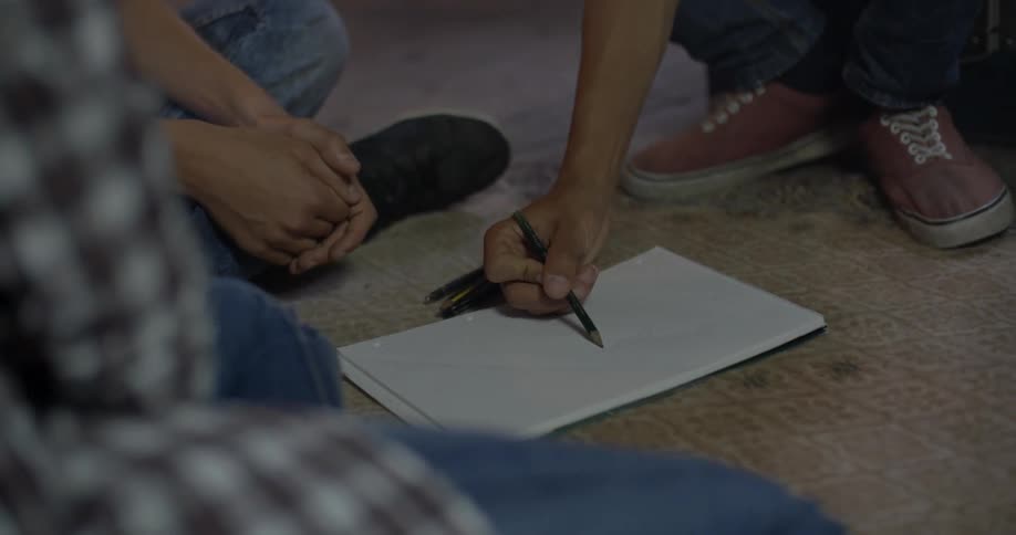 Three people sit on the floor writing in a notebook
