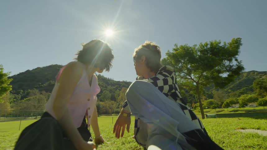 Man and woman sitting on a small hill filled with grass on a sunny day