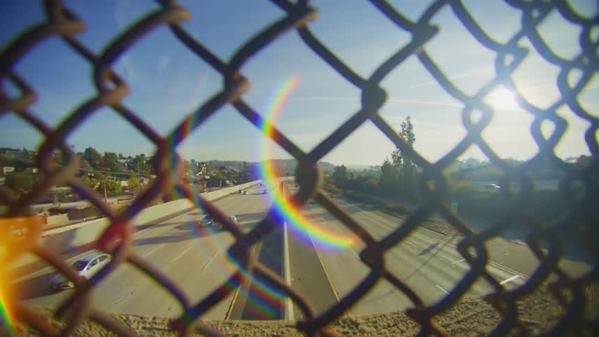 Closeup of a fence on a viaduct overlooking a highway with vehicle traffic and the reflection of sunlight