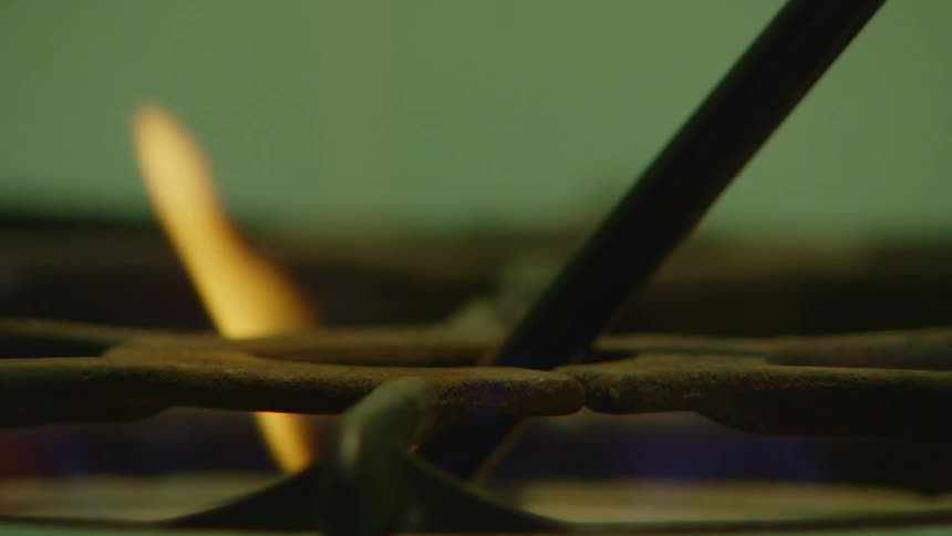 A lighter with a flame at the end lighting the mouth of a stove