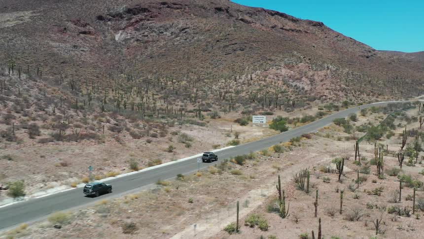 Cars traveling along a mountainous road in the desert during the day