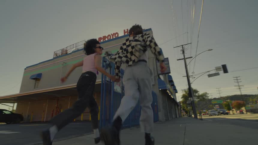 A man and a woman run down a sidewalk in a town or suburb