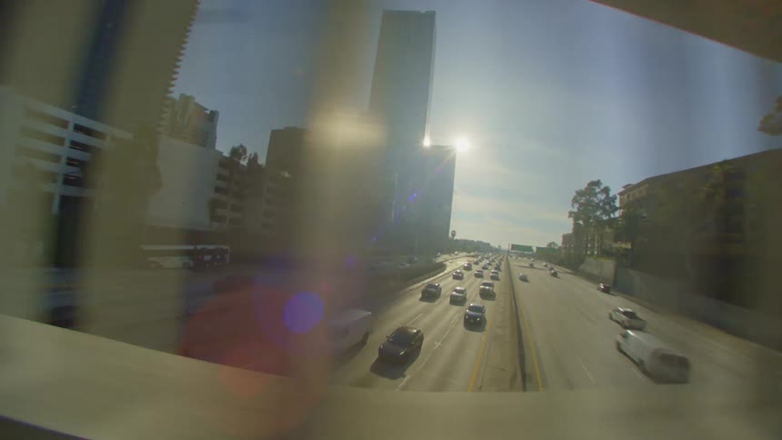 Traffic on highway bordered by buildings passes under bridge on a sunny day
