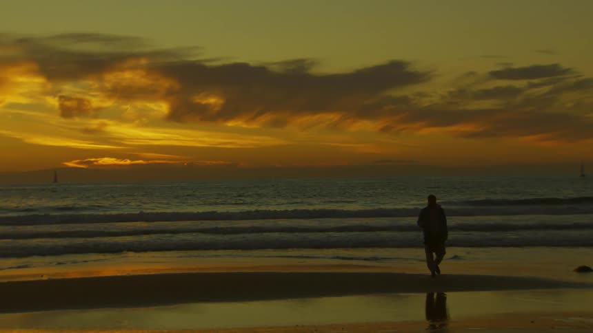 A person walking by the sea during sunset