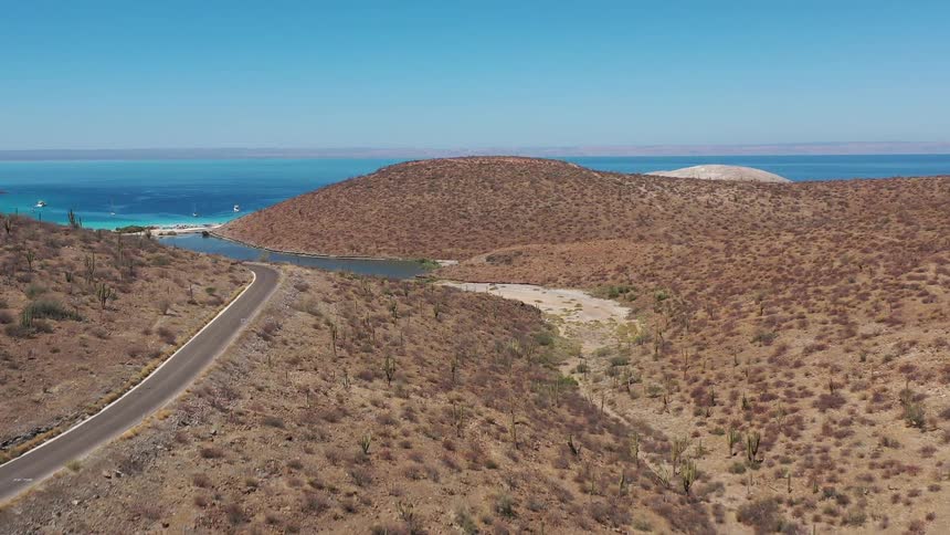 Aerial panorama of mountain ranges and a road with a turquoise beach in front