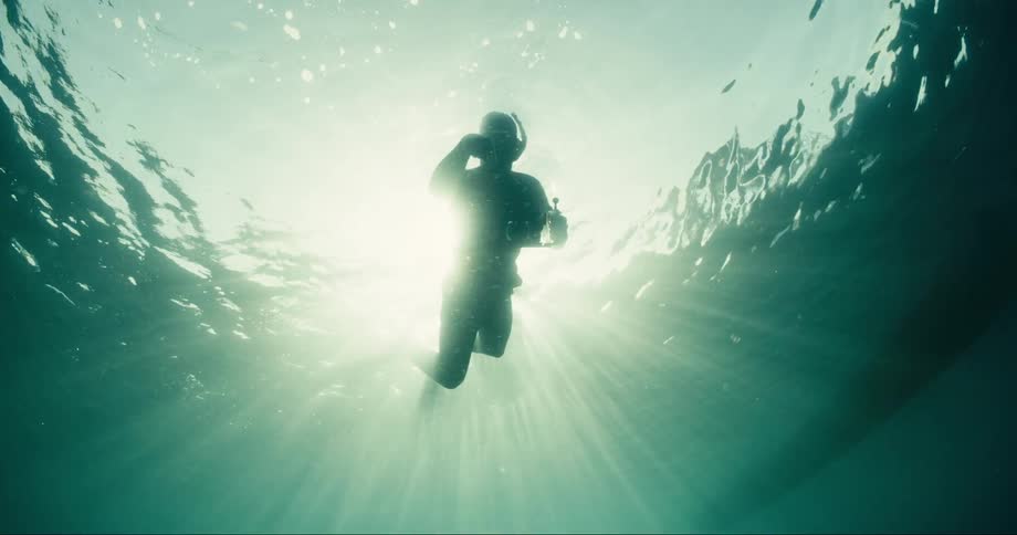 Diver in the sea using a professional camera and the suns reflection on him