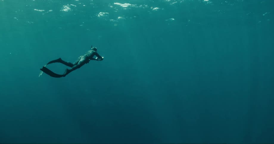 Free diver swims under water in blue ocean