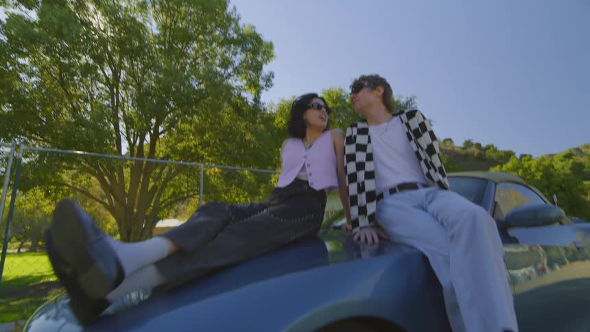 A young couple sit on the hood of a car