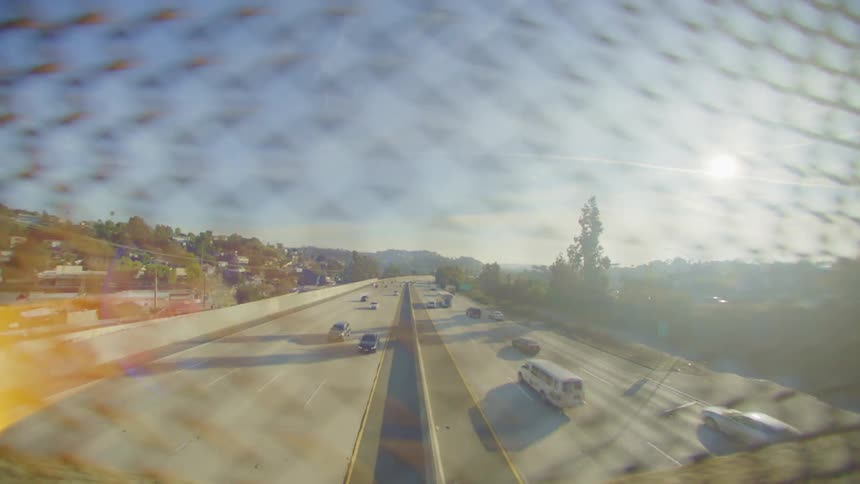 Fence on a viaduct overlooking a highway with vehicle traffic and the reflection of sunlight