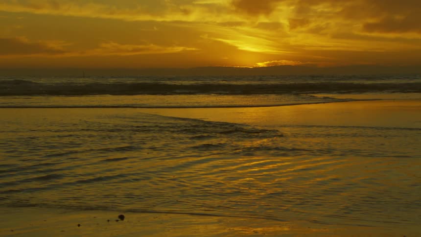 A beach is shown at dusk with small waves crashing on the shore
